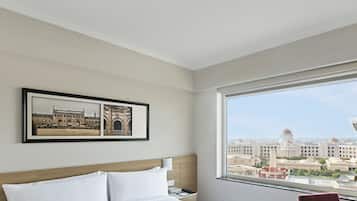 A hotel room with a large window, a bed with white linens, a framed picture of a building, and a nightstand with a phone and a book.