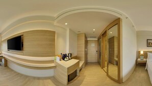 A modern hotel room with a curved seating area, a flat-screen TV, a wooden cabinet, a glass door closet, and a bedside table with a lamp. - Fairfield By Marriott Lucknow (Lucknow)