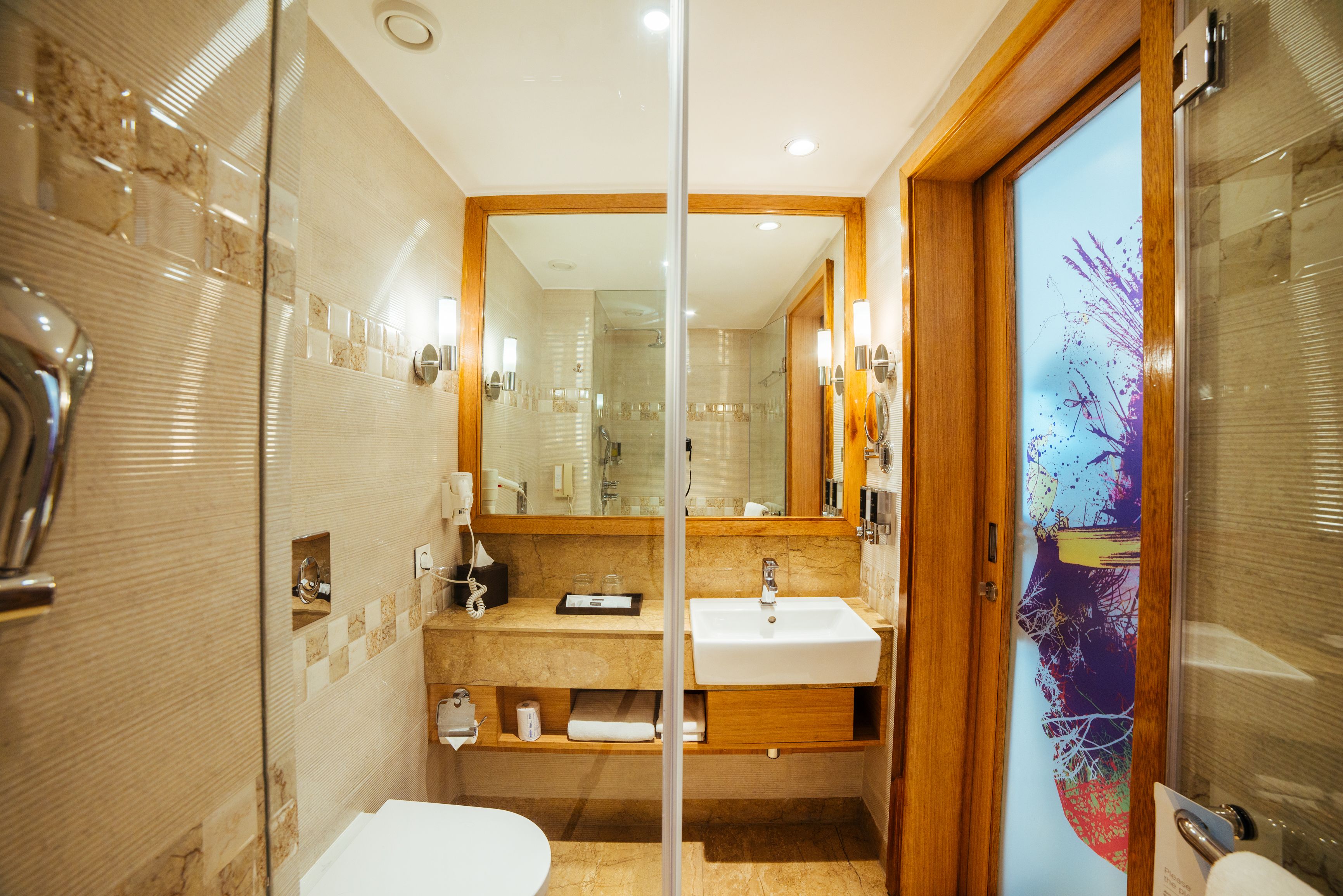 A modern bathroom with a glass shower enclosure, a wooden vanity, and a large mirror.