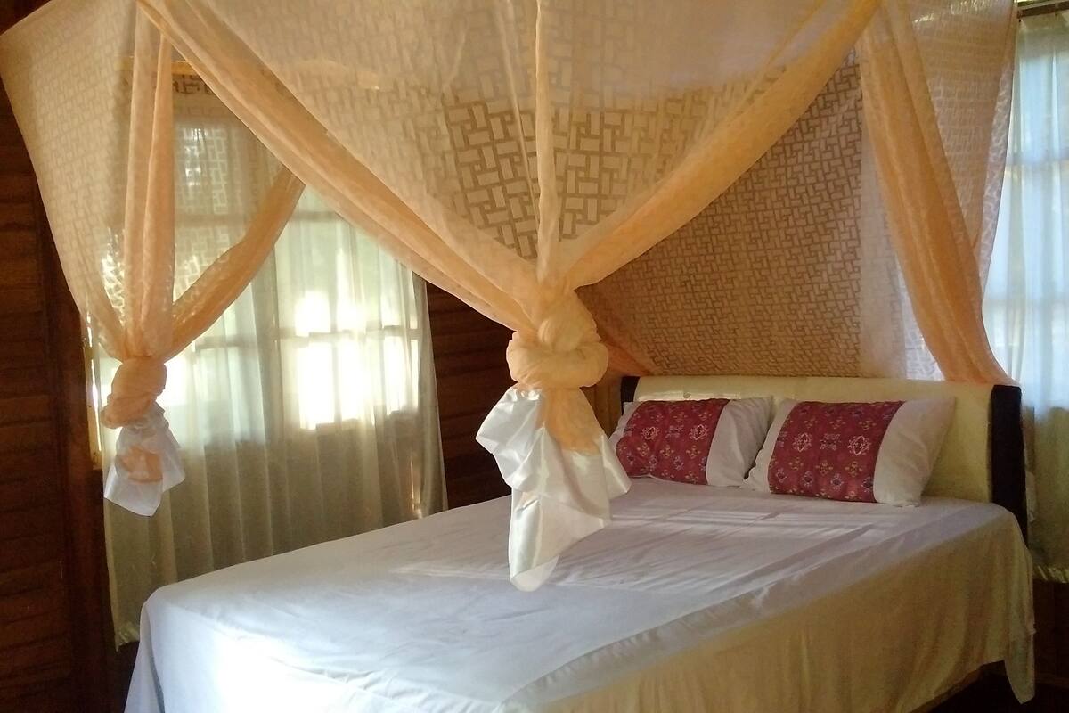 Una cama con dosel, almohadas y un diseño tejido en la pared.