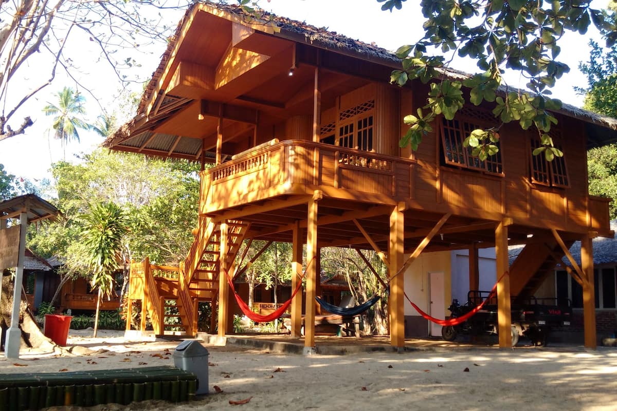 Una estructura de madera con balcón, una hamaca y una escalera que lleva al nivel superior.