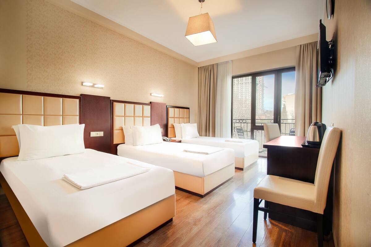A hotel room with two beds, a desk, a chair, and a large window.