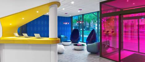A modern reception area with a curved desk, seating with bean bags, and a glass wall with a pink-lit interior.