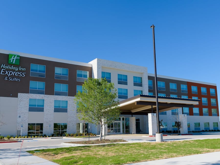 A Holiday Inn Express & Suites building with a modern design, featuring a mix of brick and glass facade, a covered entrance, and a landscaped front yard.