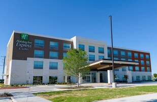 Edificio de Holiday Inn Express & Suites con un diseño moderno, que presenta una fachada mixta de ladrillo y vidrio, una entrada cubierta y un jardín delantero ajardinado.