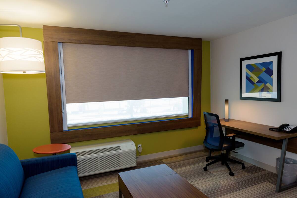 A modern room with a large window, a desk, a chair, a sofa, and a radiator.