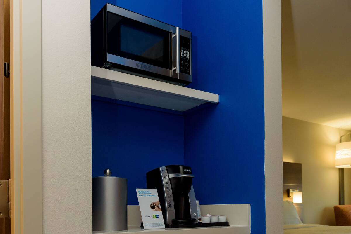 A compact hotel room with a blue accent wall, a microwave, a coffee maker, and a mini-fridge.