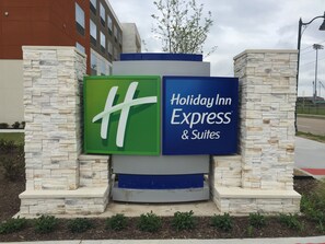 A Holiday Inn Express & Suites sign with a green and blue logo, surrounded by stone pillars and a landscaped area. - Holiday Inn Express & Suites McKinney - Frisco East by IHG (McKinney)