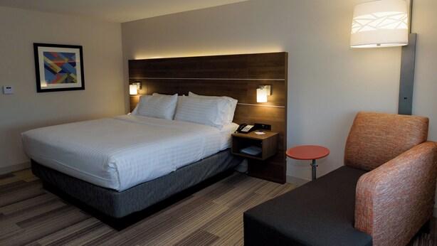 A hotel room with a bed, bedside table, lamp, and a chair. - Holiday Inn Express & Suites McKinney - Frisco East by IHG (McKinney)