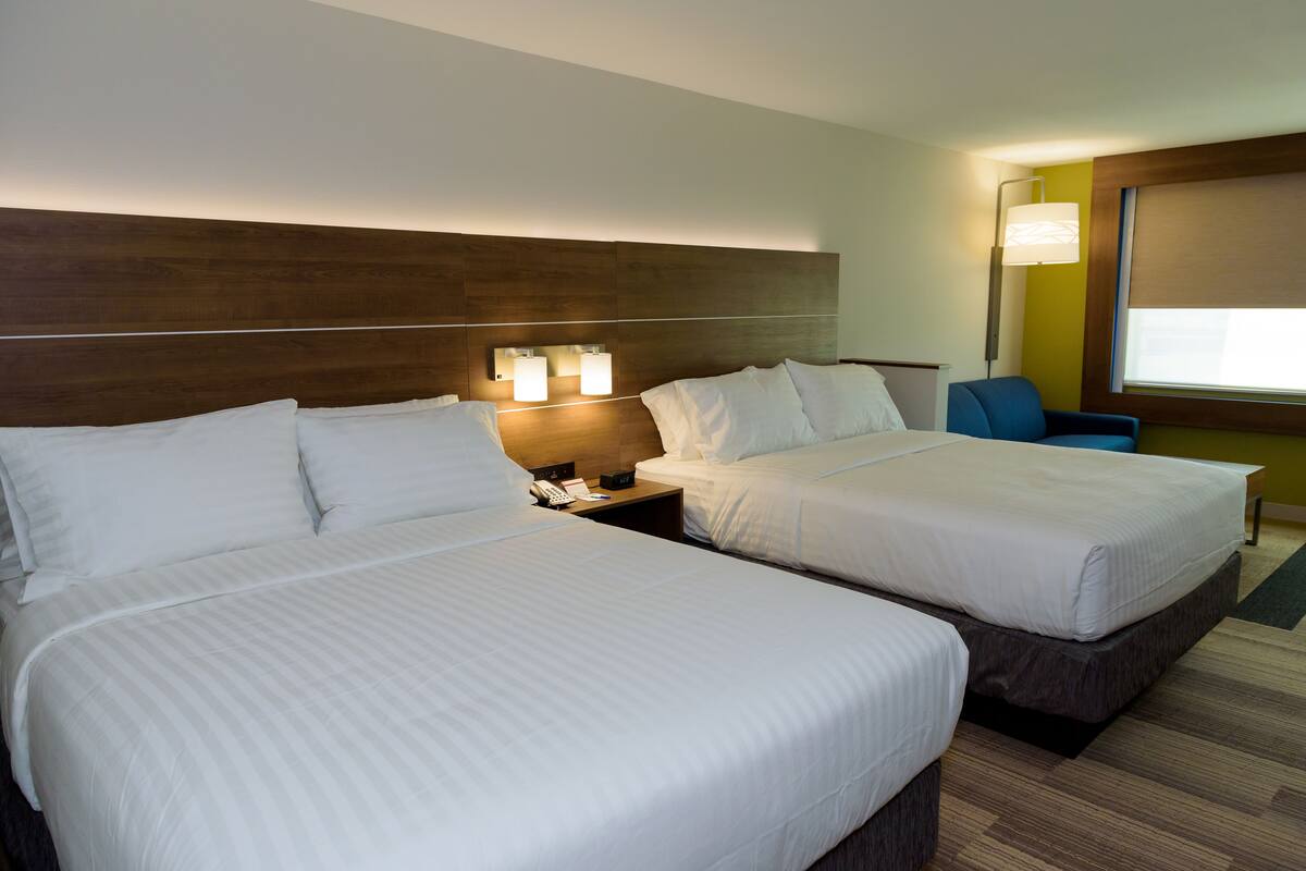 A hotel room with two beds, a nightstand with a phone and lamp, and a window with a view.