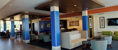 A spacious lobby with a high ceiling, seating areas, and a television screen.