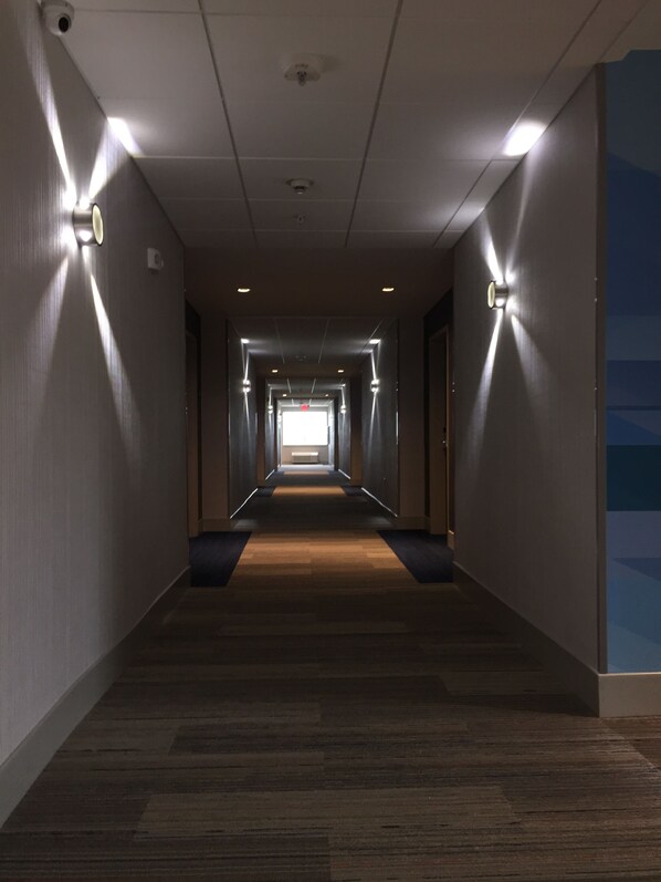 A long, narrow hallway with a carpeted floor, recessed lighting, and a plain wall on one side.