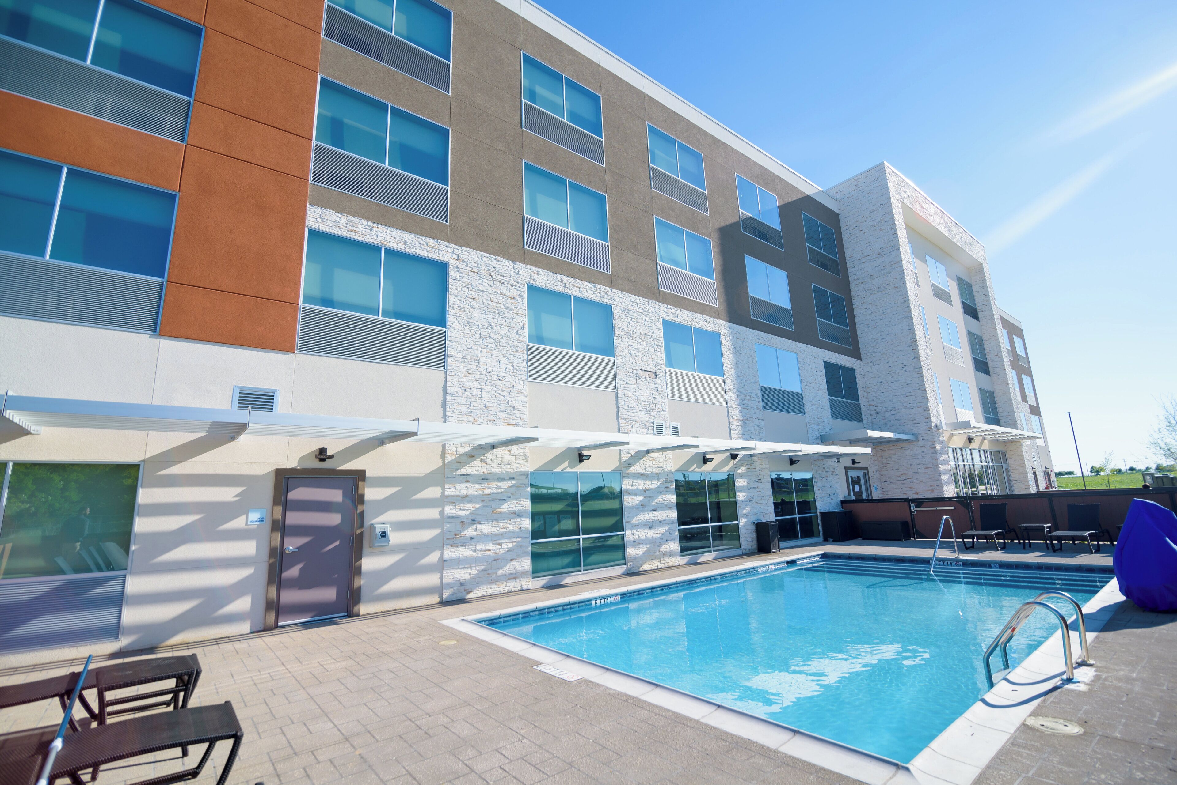 Un edificio moderno con piscina, zona de estar exterior y cielo despejado.