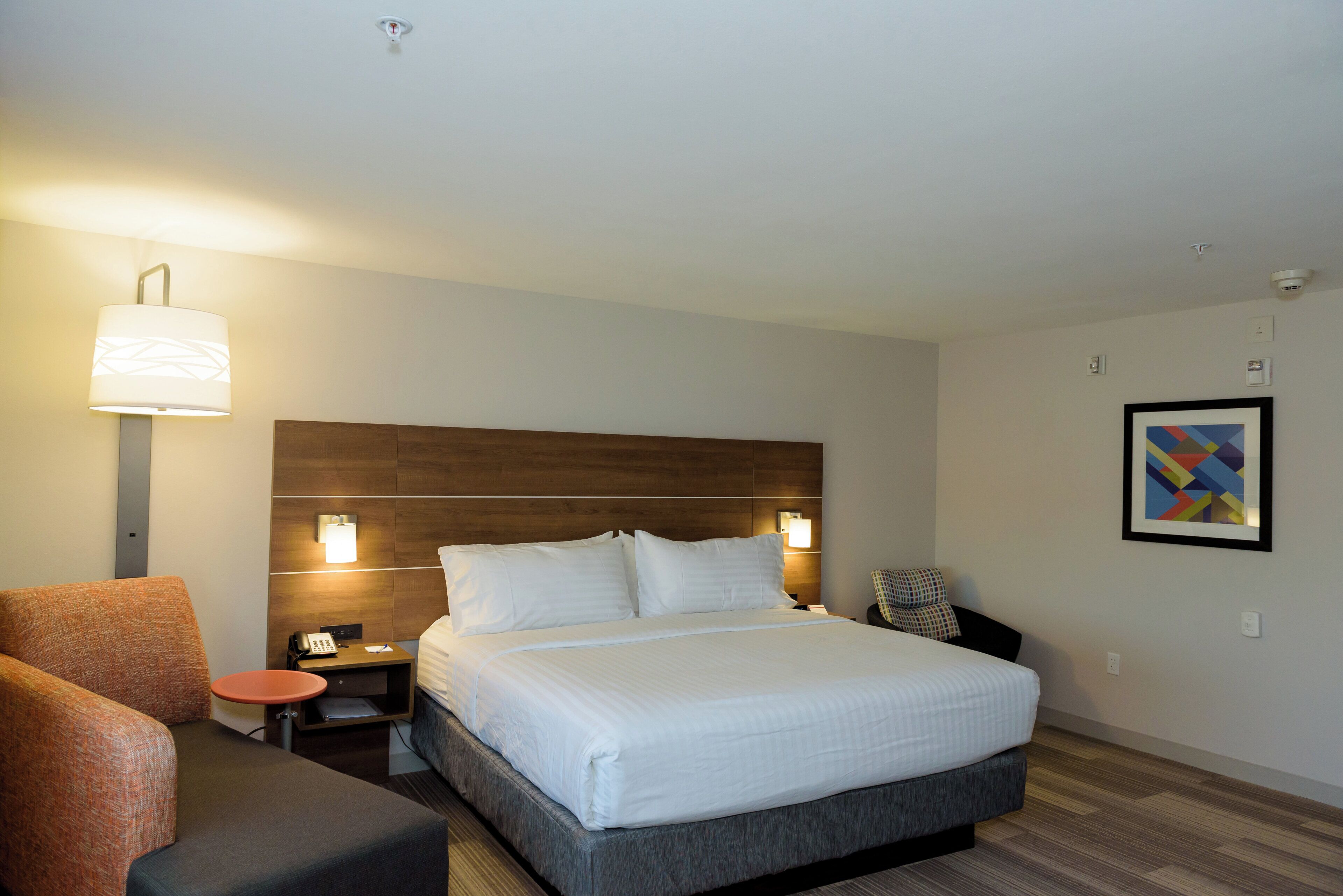 A hotel room with a large bed, bedside tables, a desk, a chair, and a wall-mounted lamp.