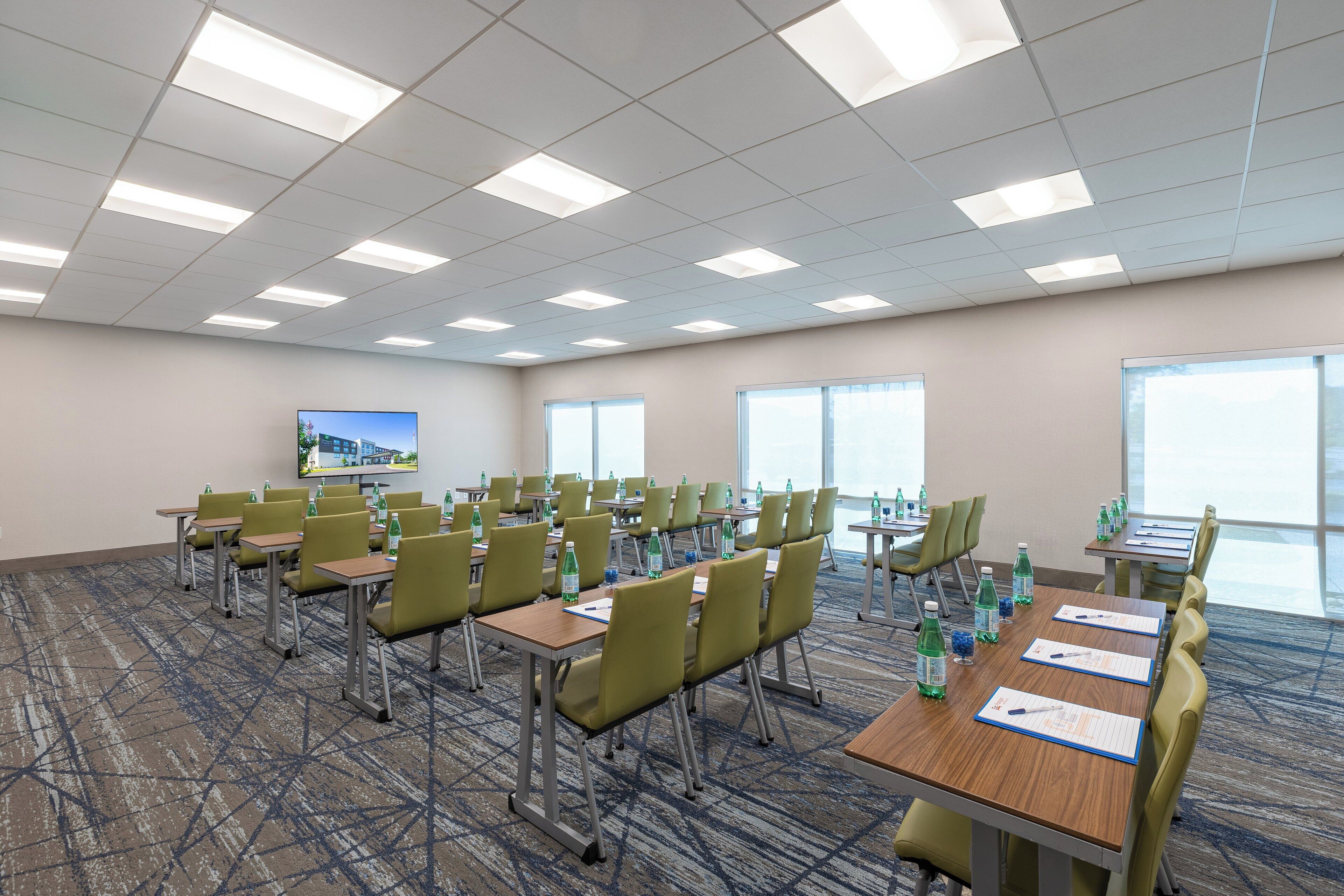 A conference room with multiple tables and chairs, equipped with water bottles and papers, and a television on the wall.