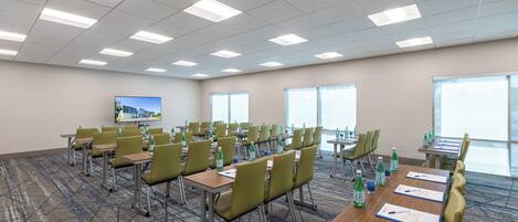 A conference room with multiple tables and chairs, equipped with water bottles and papers, and a television on the wall.
