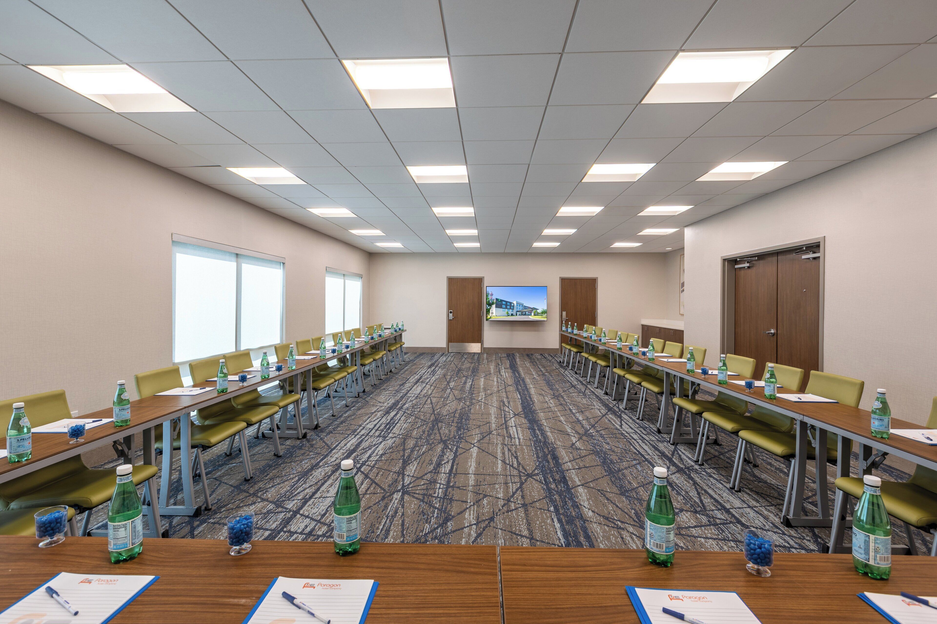 Un salón de conferencias con mesas largas, sillas y botellas de agua.