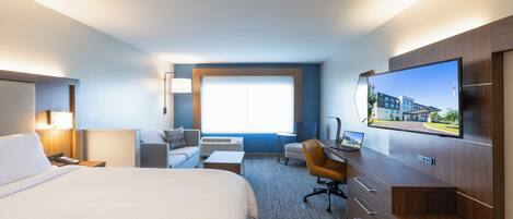 A hotel room with a large bed, a desk, a chair, a TV, and a window with a view of buildings.