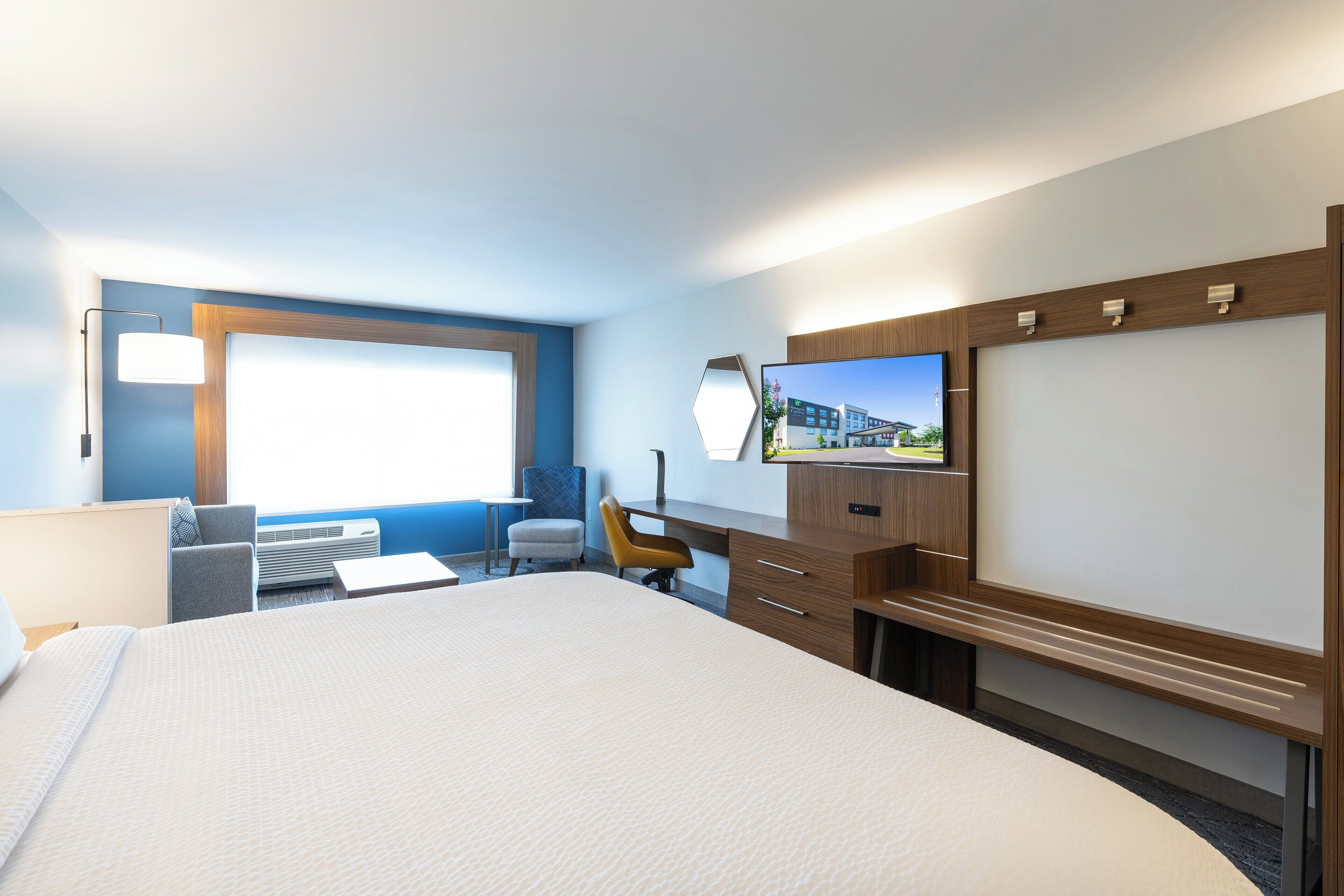 Habitación de hotel con una cama grande, un escritorio, una silla, un televisor y una ventana con vistas a edificios.