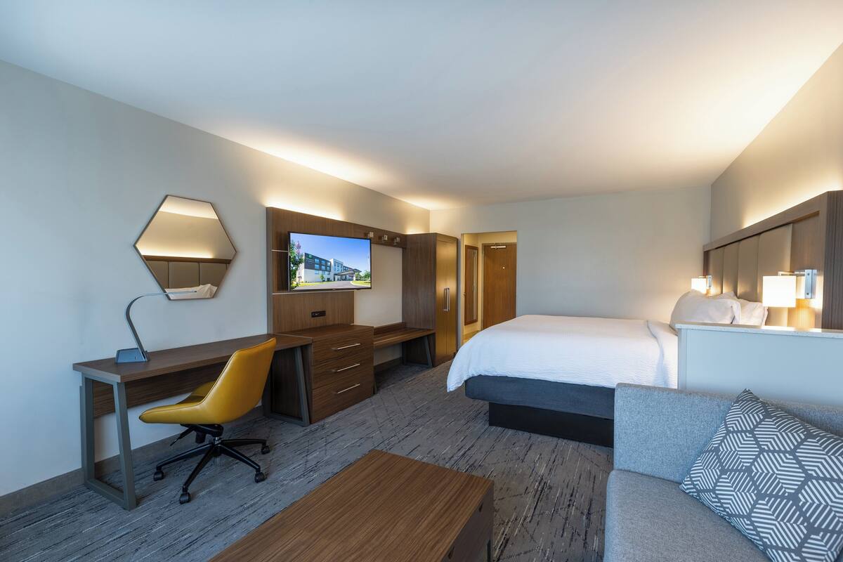 A hotel room with a bed, a desk, a chair, a TV, and a sofa.