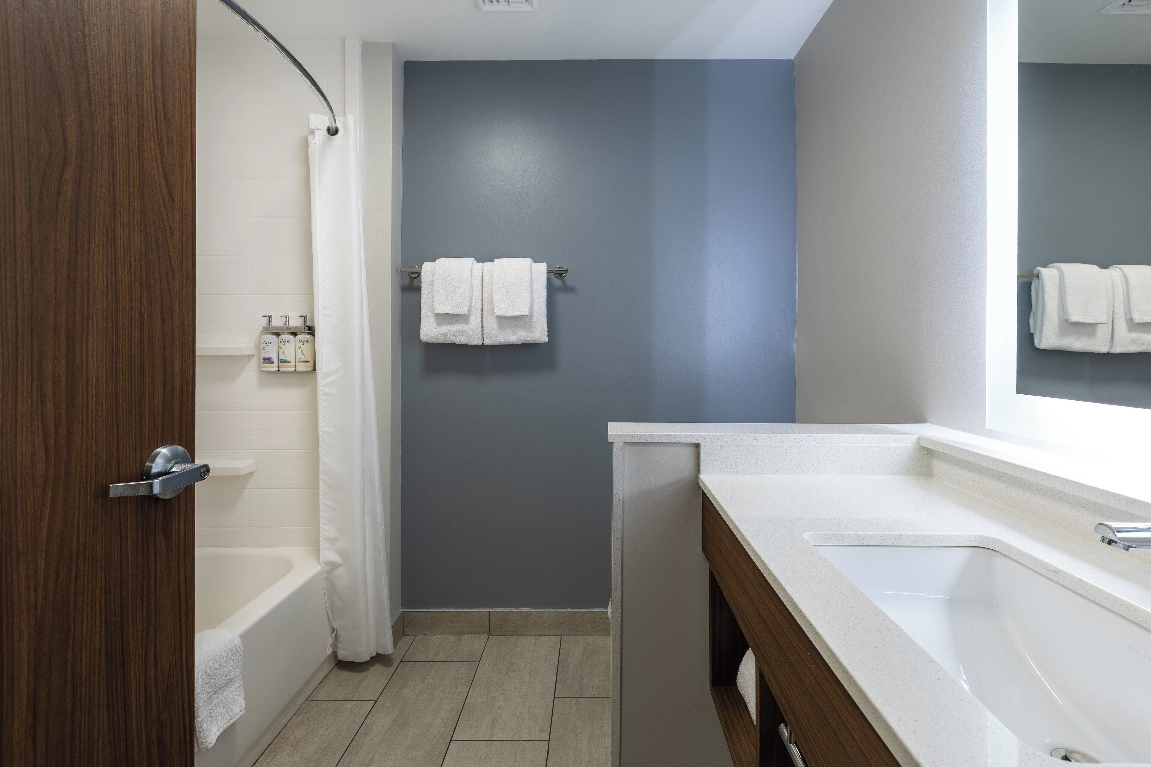 A bathroom with a bathtub, a sink, and a mirror. There are towels hanging on the wall and a shower curtain.