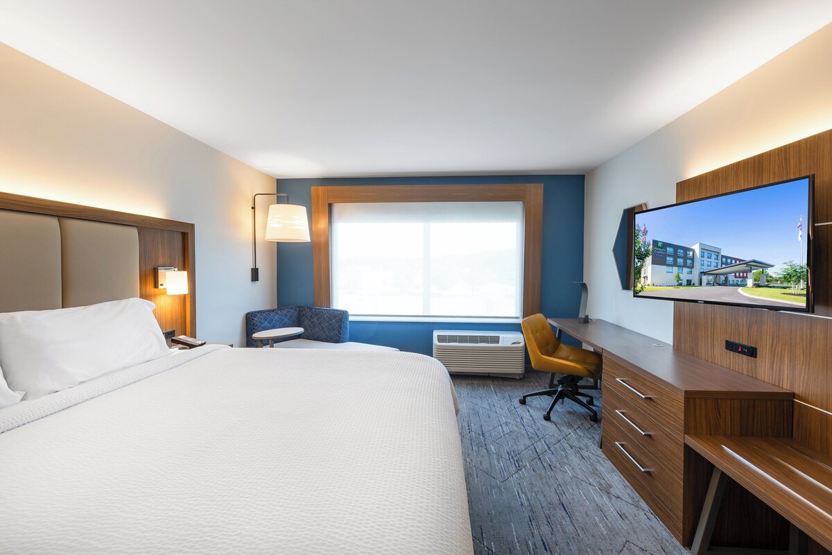 Habitación de hotel con una cama grande, un escritorio, una silla, un televisor y una ventana con vistas a edificios.