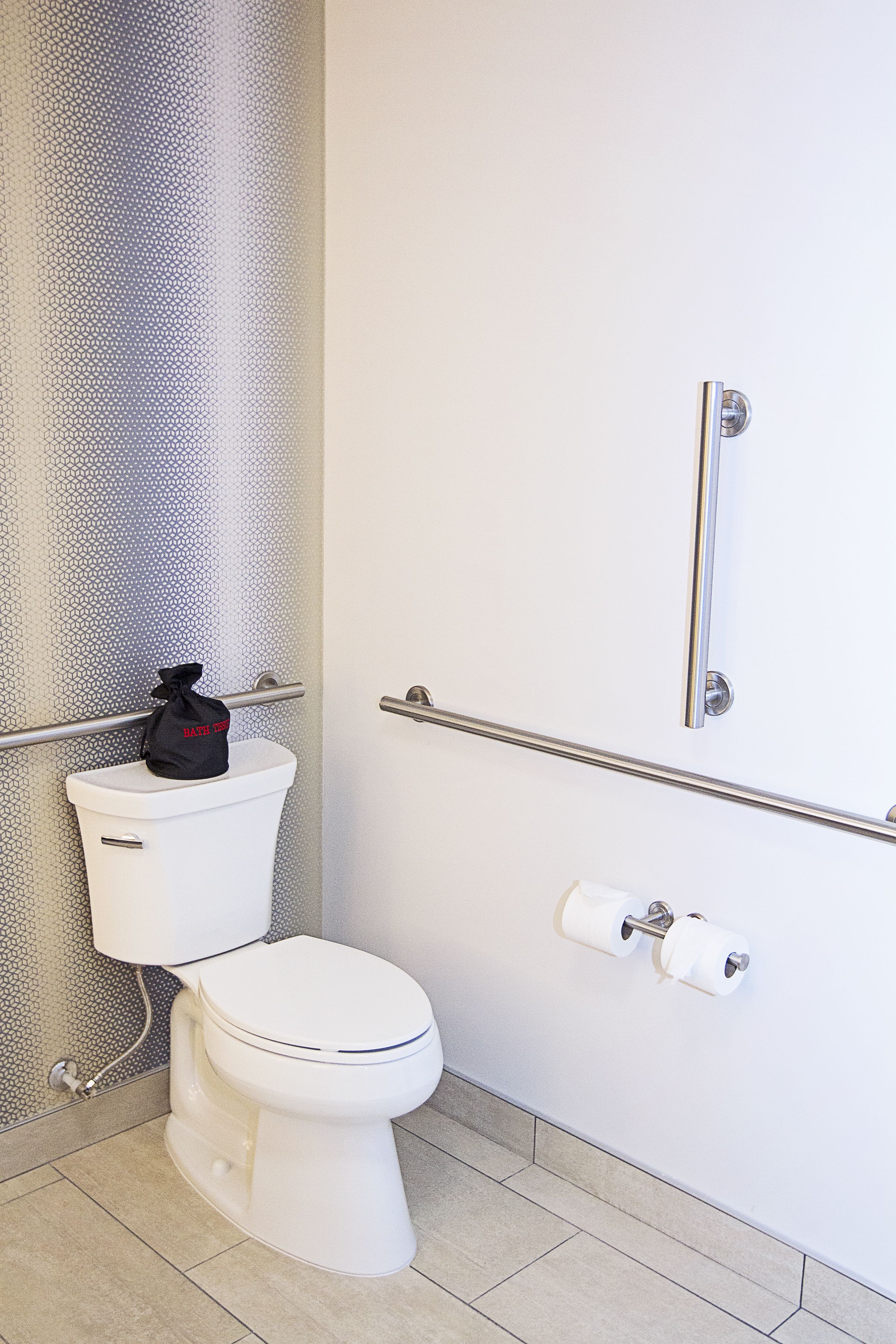 A modern bathroom with a white toilet, a handrail, and a toilet paper holder.