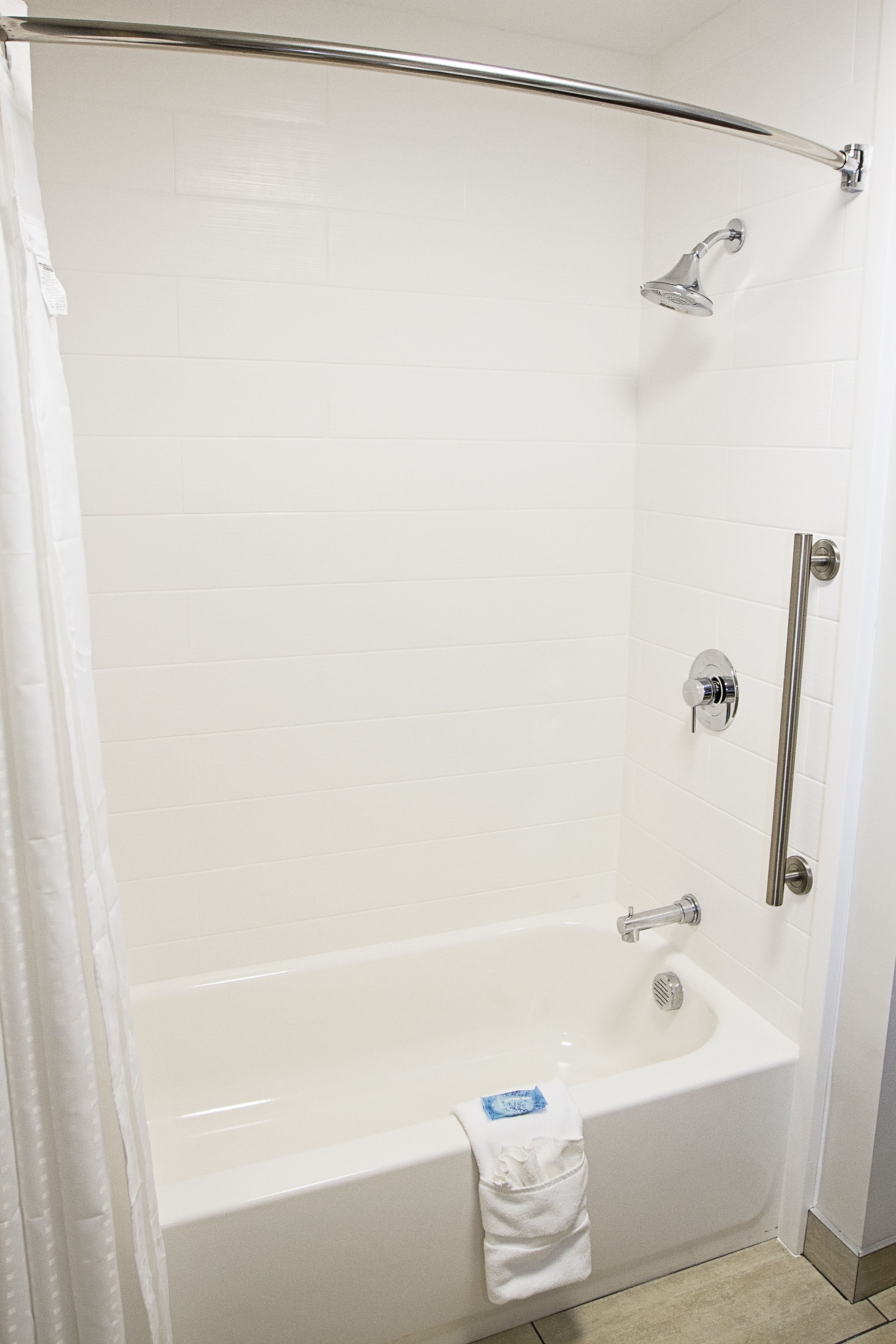 A white bathroom with a bathtub, shower, and handrail.