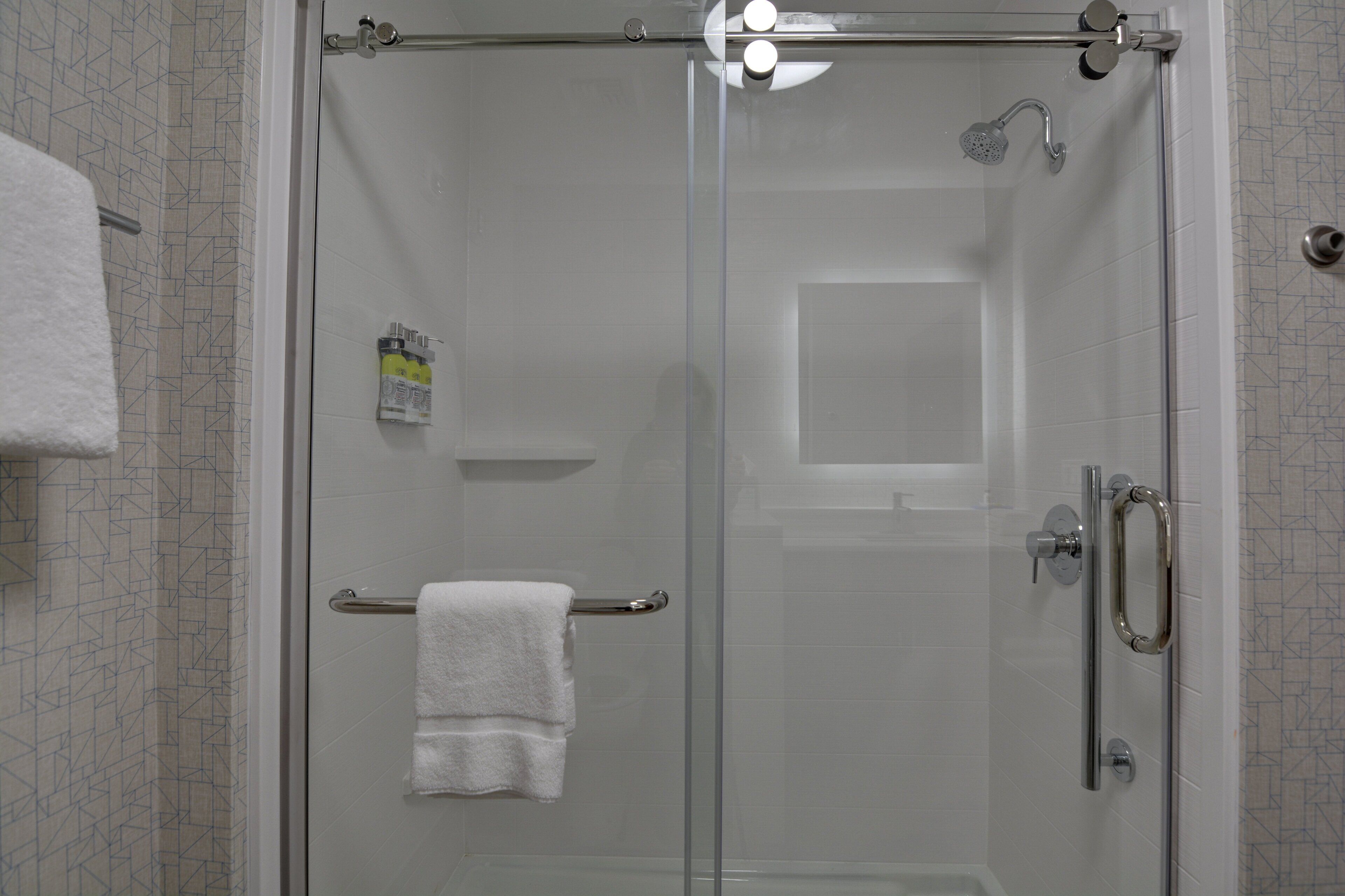 A glass-enclosed shower with a towel rack and a handheld showerhead.