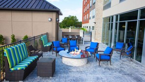 An outdoor patio area with wicker furniture, a central fire feature, and a view of the building's exterior. - Holiday Inn Express & Suites Greenwood Mall by IHG (Greenwood)