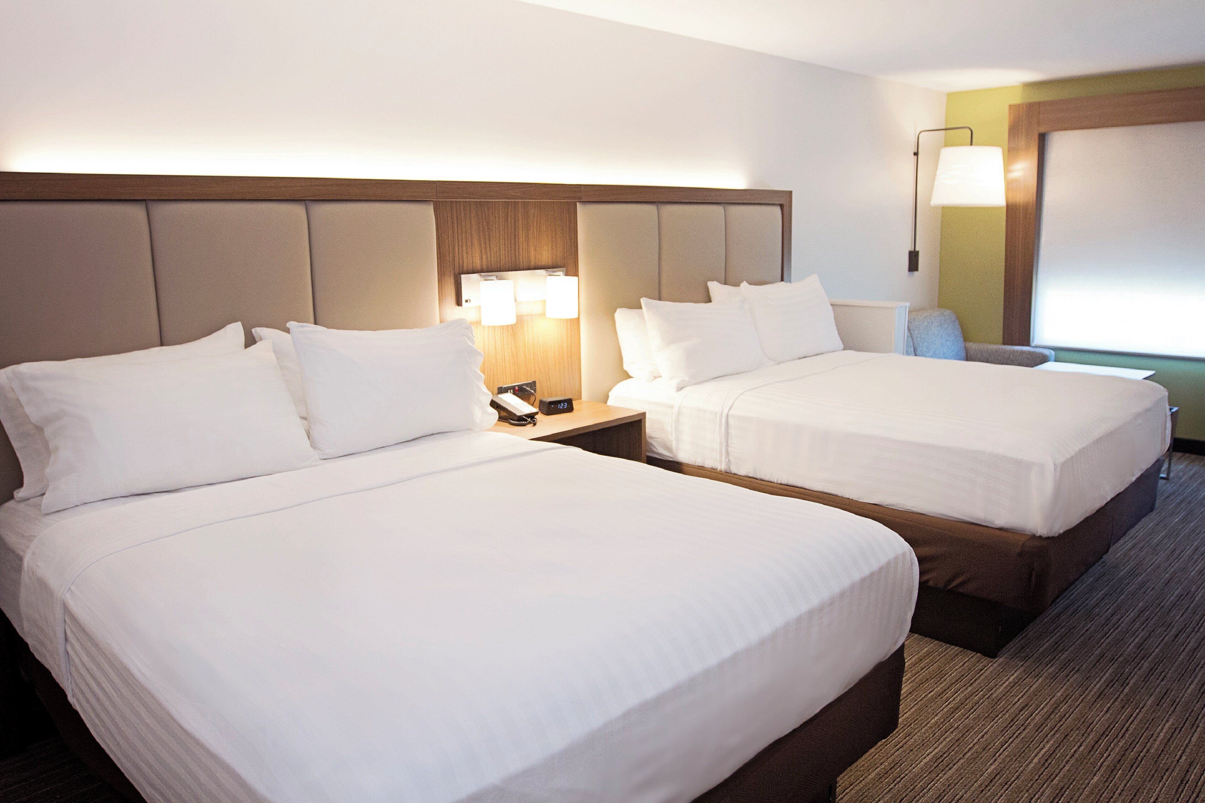 Une chambre d’hôtel avec deux lits, une table de chevet avec une lampe et un luminaire fixé au mur.