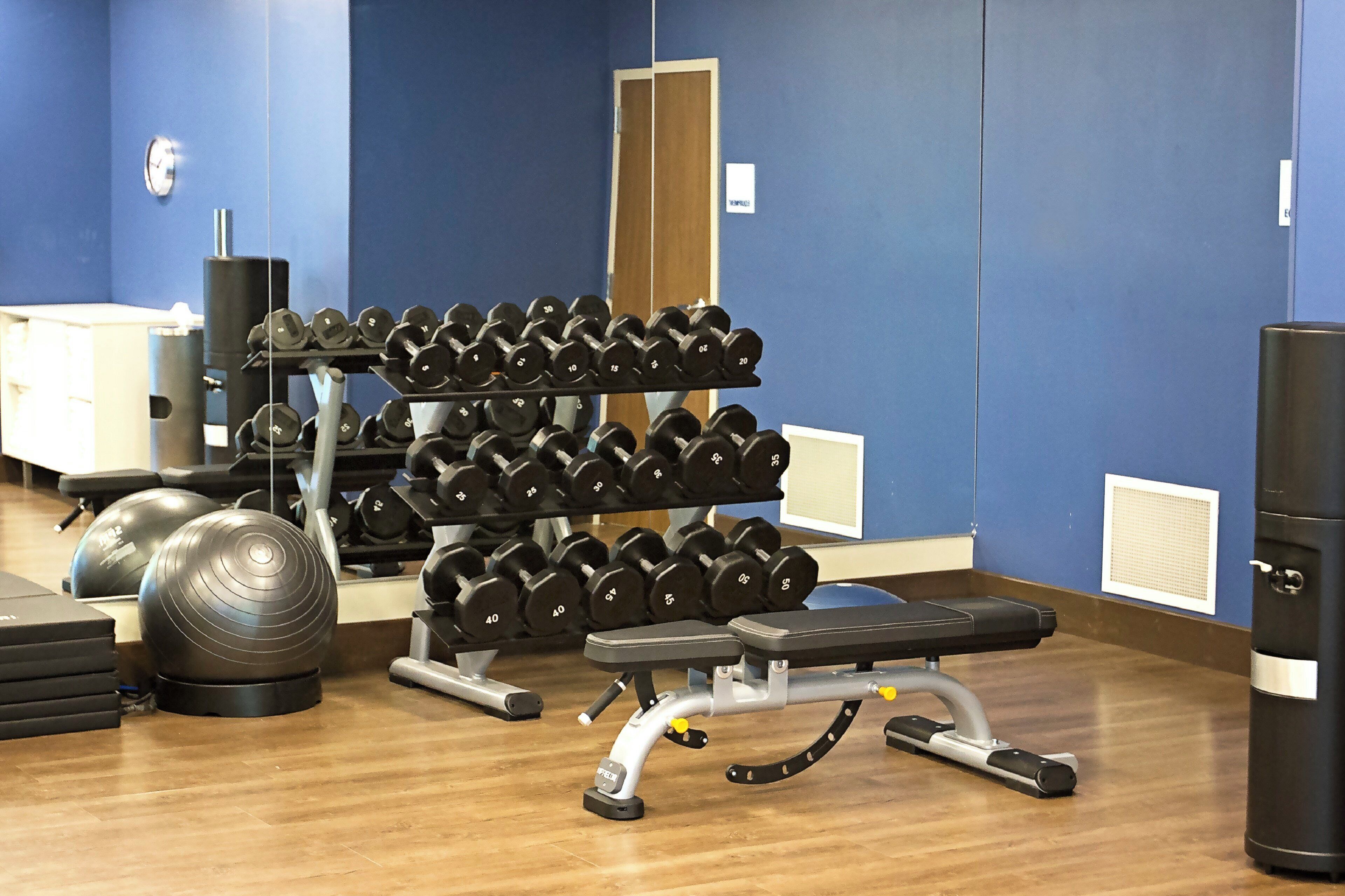Un gimnasio con una banca, mancuernas y pelotas de ejercicio.