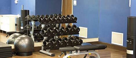 Un gimnasio con una banca, mancuernas y pelotas de ejercicio.