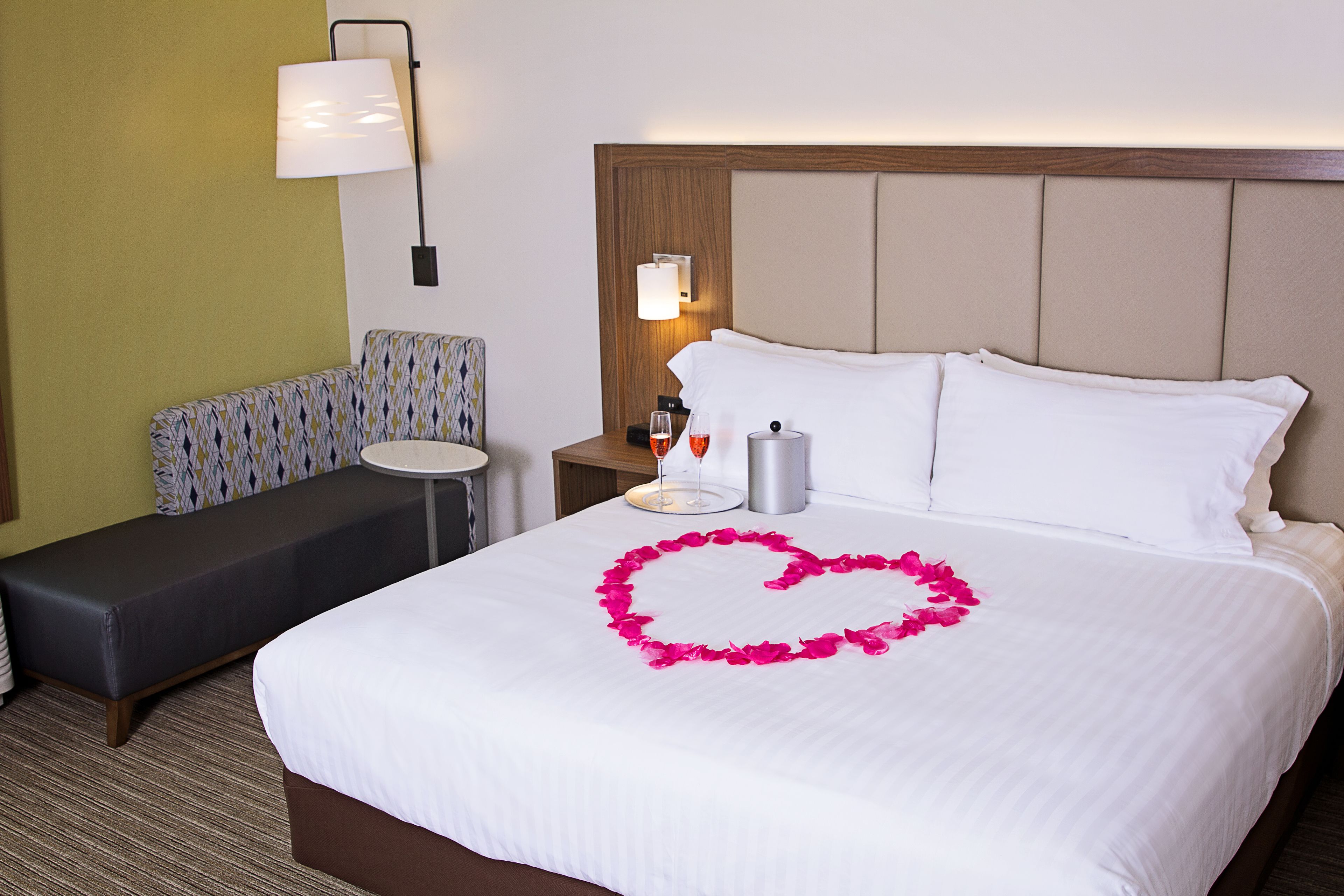 A hotel room with a bed, a bedside table, a lamp, and a bench.