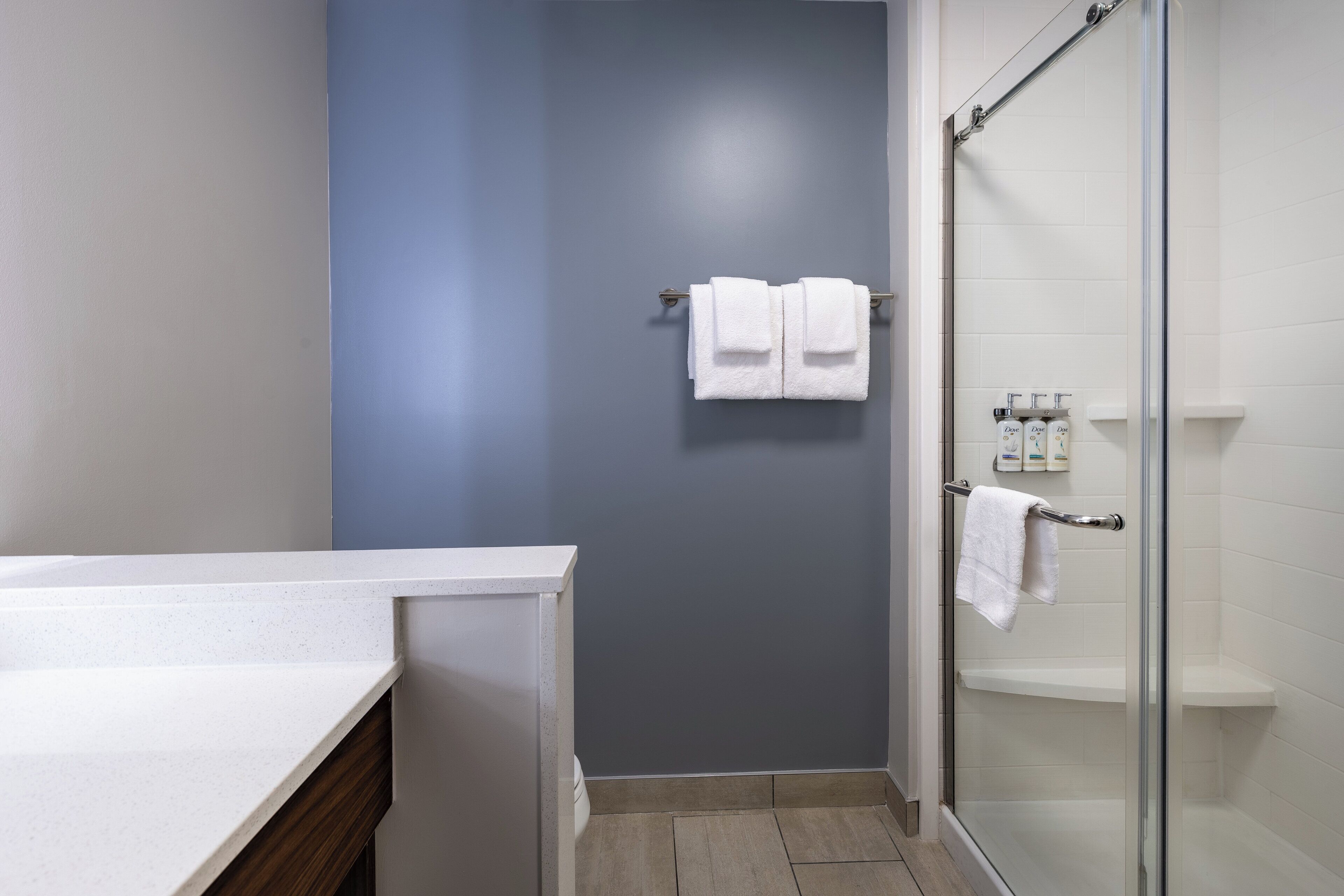 A bathroom with a shower, a towel rack with two towels, and a shelf with toiletries.