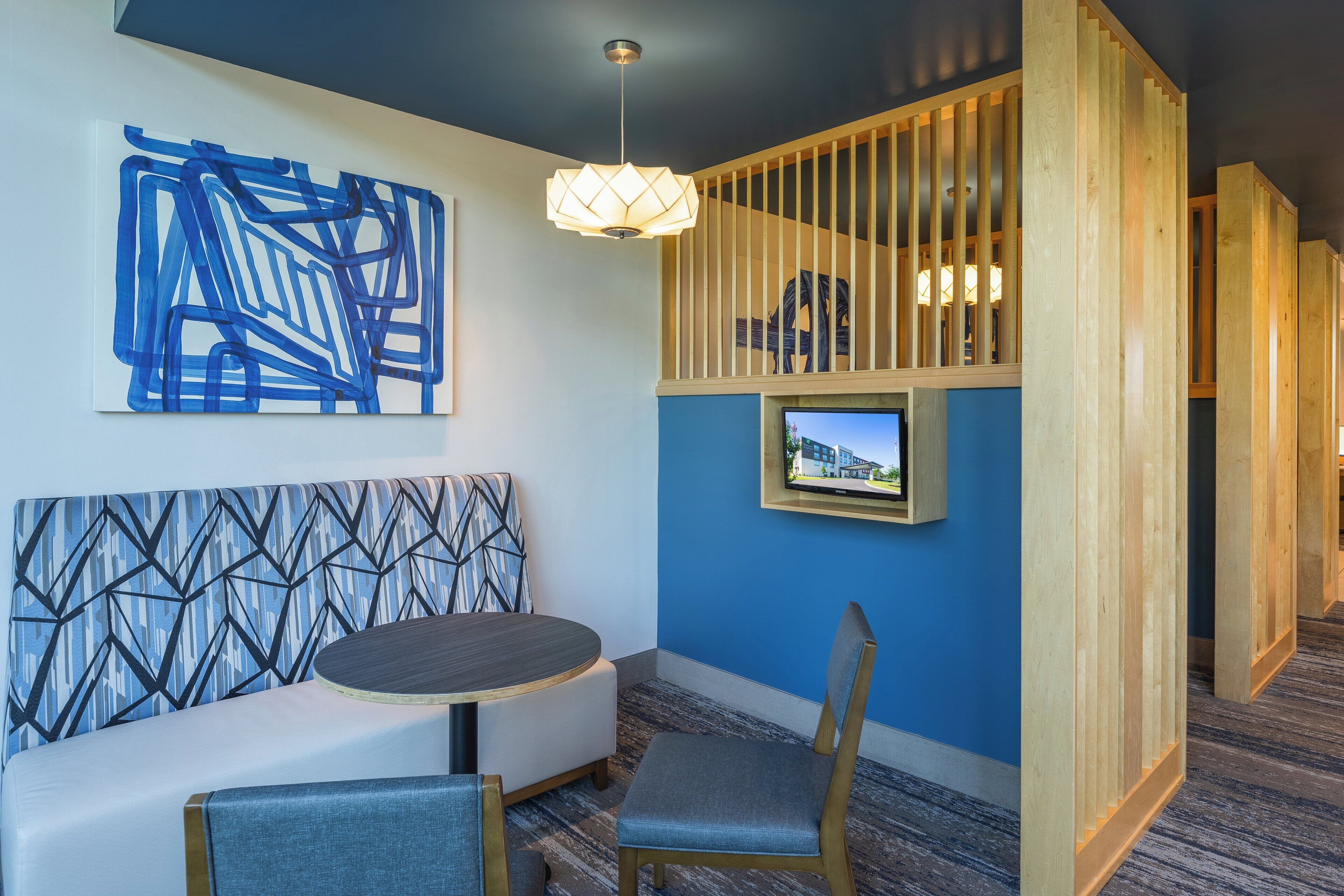 A modern room with a blue and white geometric wall design, a round table with a chair, a television mounted on the wall, and a wooden partition with vertical slats.