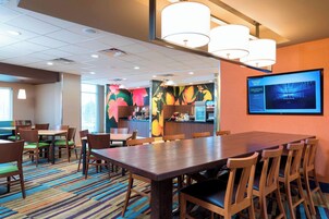 Un comedor de hotel con una amplia mesa de madera, varias sillas, una alfombra colorida y un televisor montado en la pared.