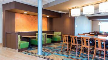 A hotel lobby with a reception desk, green seating area, and a dining area with wooden tables and chairs.