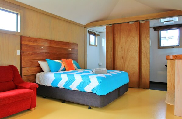 A bedroom with a bed, a red chair, and a wooden wardrobe.