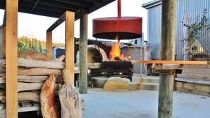 Een houtgestookte oven met houtblokken en een vuur, ondersteund door houten palen.