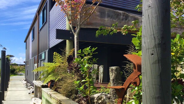 Een modern huis met twee verdiepingen, een houten terras en een metalen leuning.