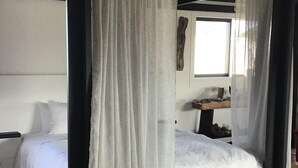 Een hemelbed met witte lakens, een houten hoofdeinde en een raam met natuurlijk licht.