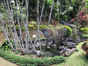 A garden with a pond, stone structures, and various plants. - Sinar Express Villa (Trawas)