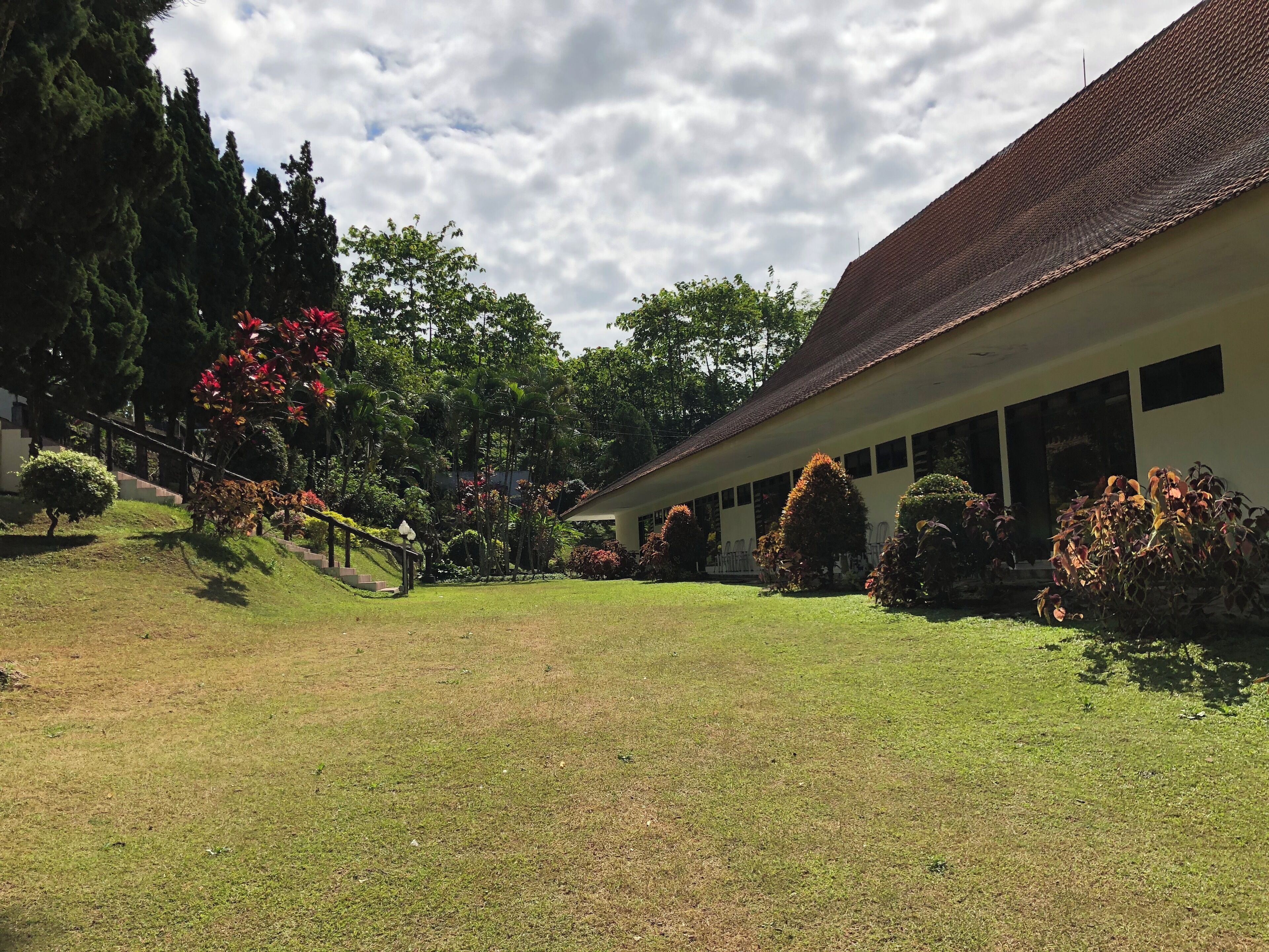 A building with a tiled roof, surrounded by well-maintained lawns and various shrubs.