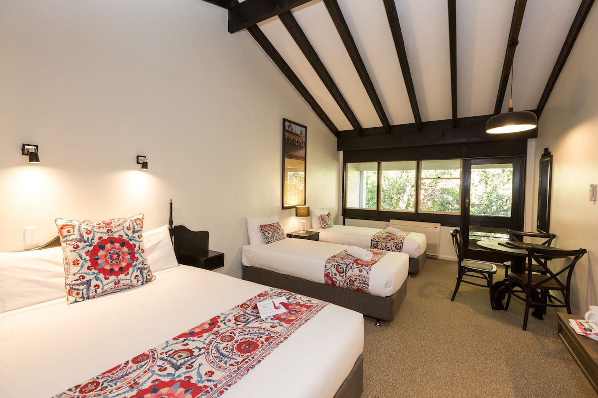 Habitación de hotel con dos camas, un escritorio y una silla. Se ve un ventanal con vistas a árboles.