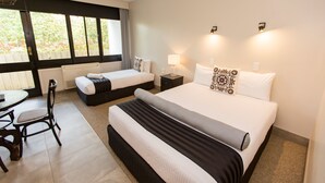 A hotel room with a large bed, a smaller bed, a desk with a chair, and a window with curtains. - The Matador (Sale)