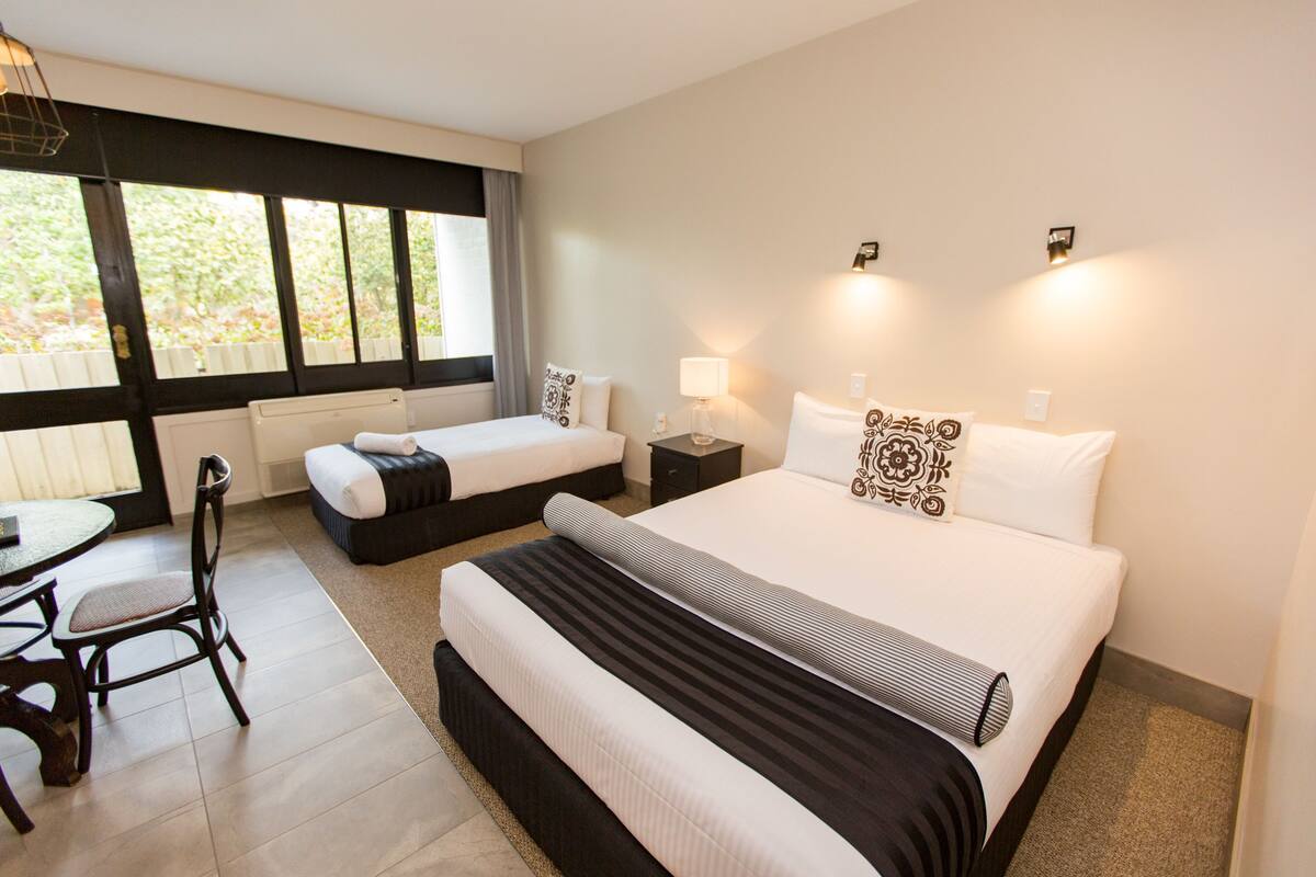 Habitación de hotel con una cama grande, una cama más pequeña, un escritorio con silla y una ventana con cortinas.