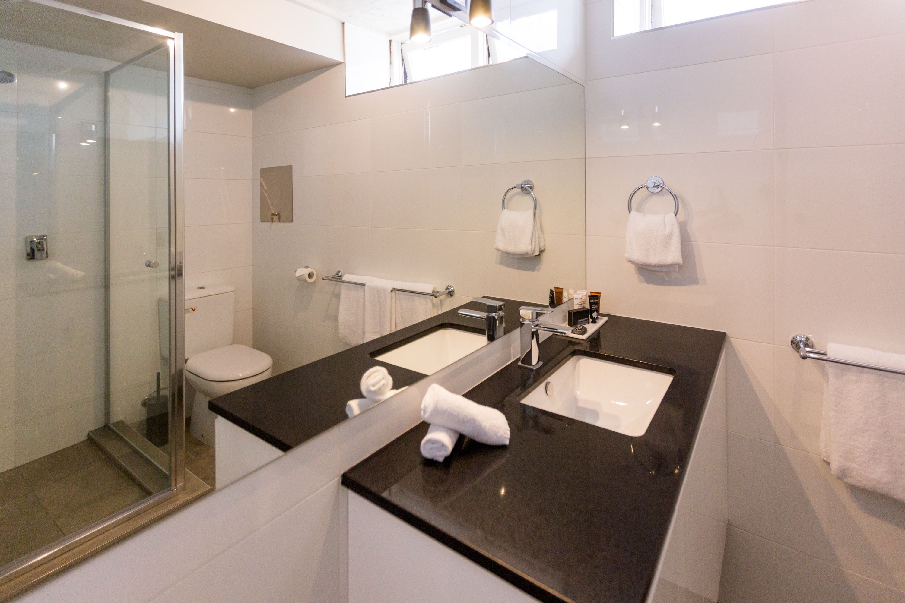 Un bagno moderno con cabina doccia in vetro, doppio lavabo e servizi igienici.