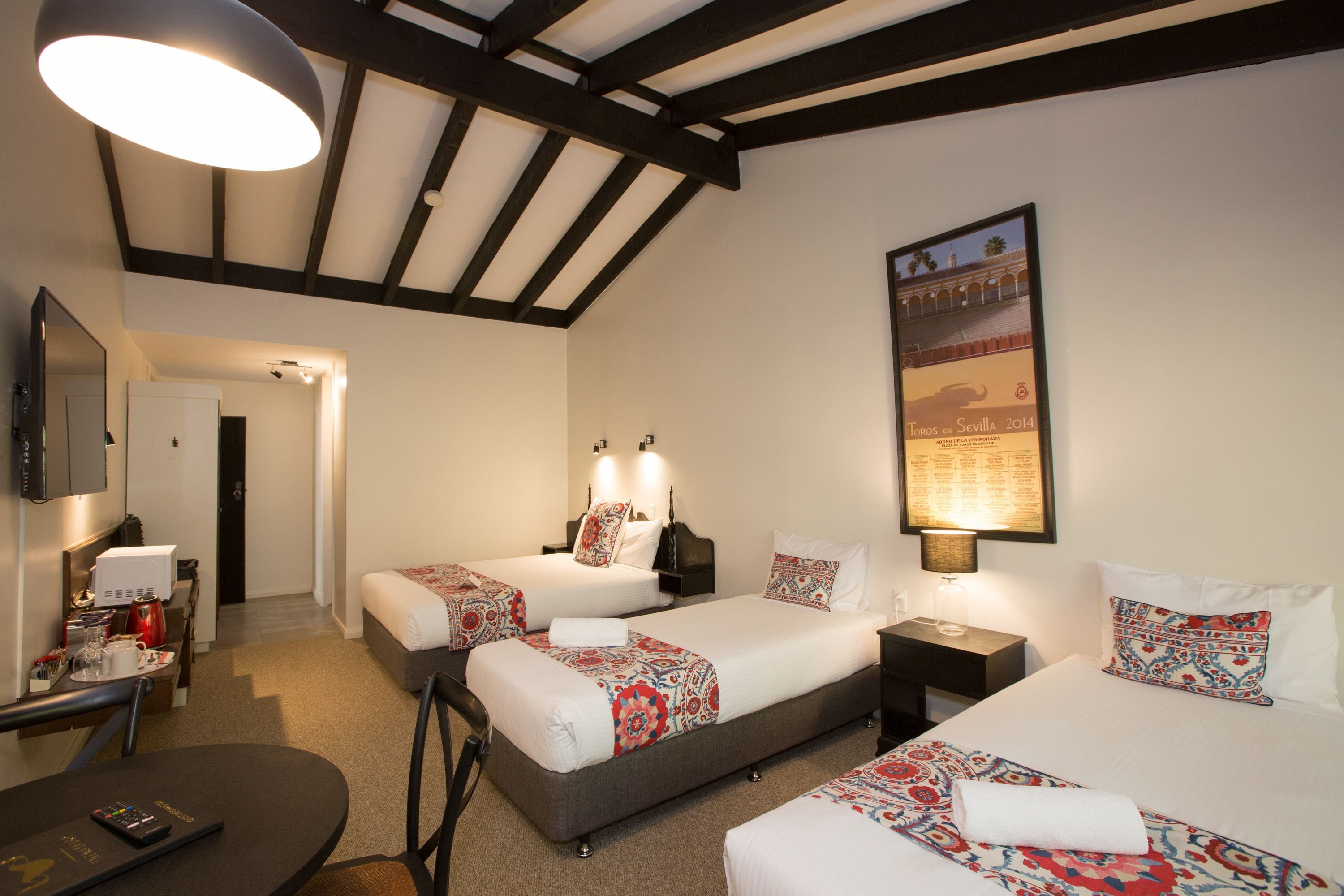 A hotel room with two beds, a desk, a chair, a TV, and a poster on the wall.