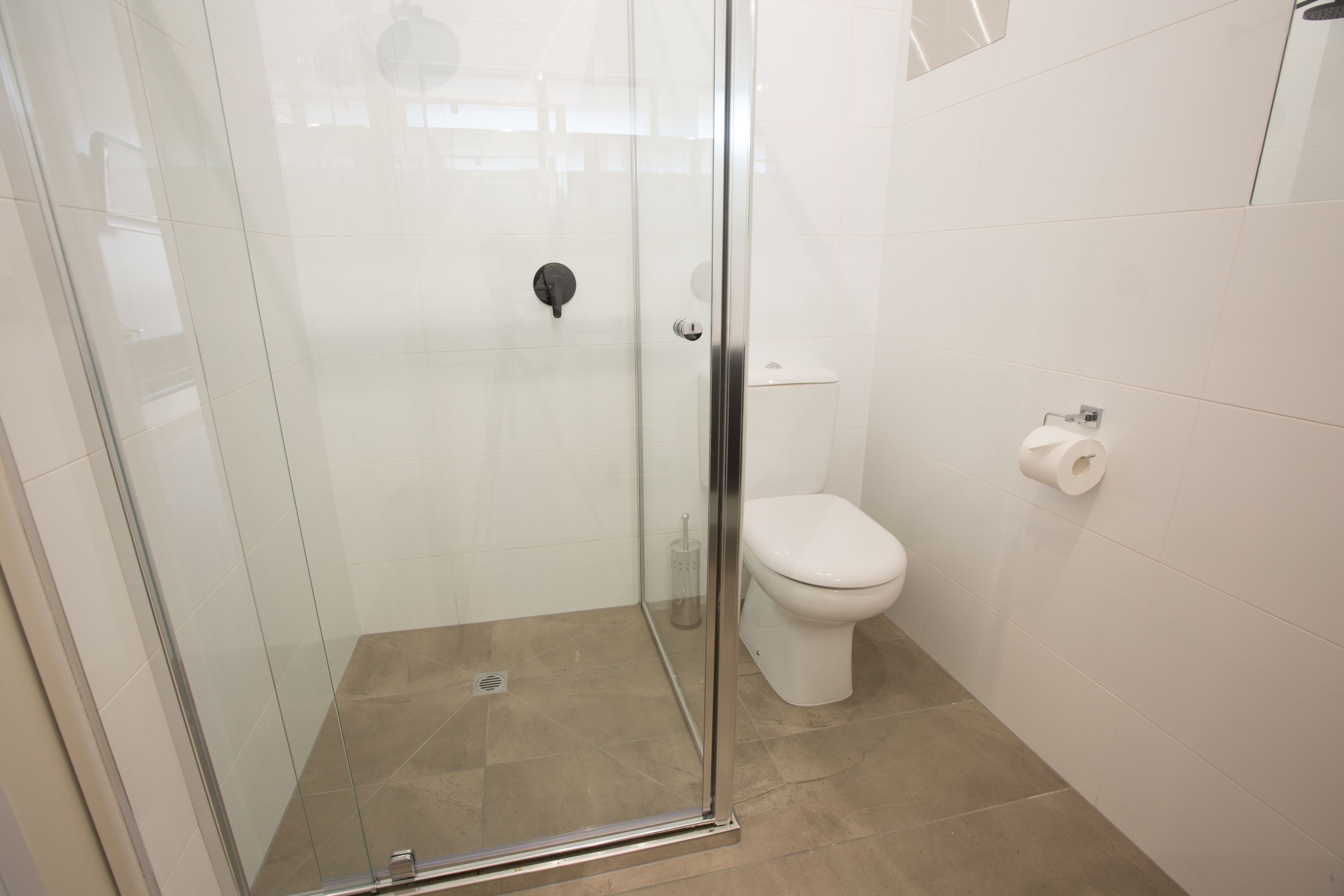 Une salle de bain moderne avec une douche à parois de verre, des toilettes blanches et un porte-rouleau de papier toilette fixé au mur.